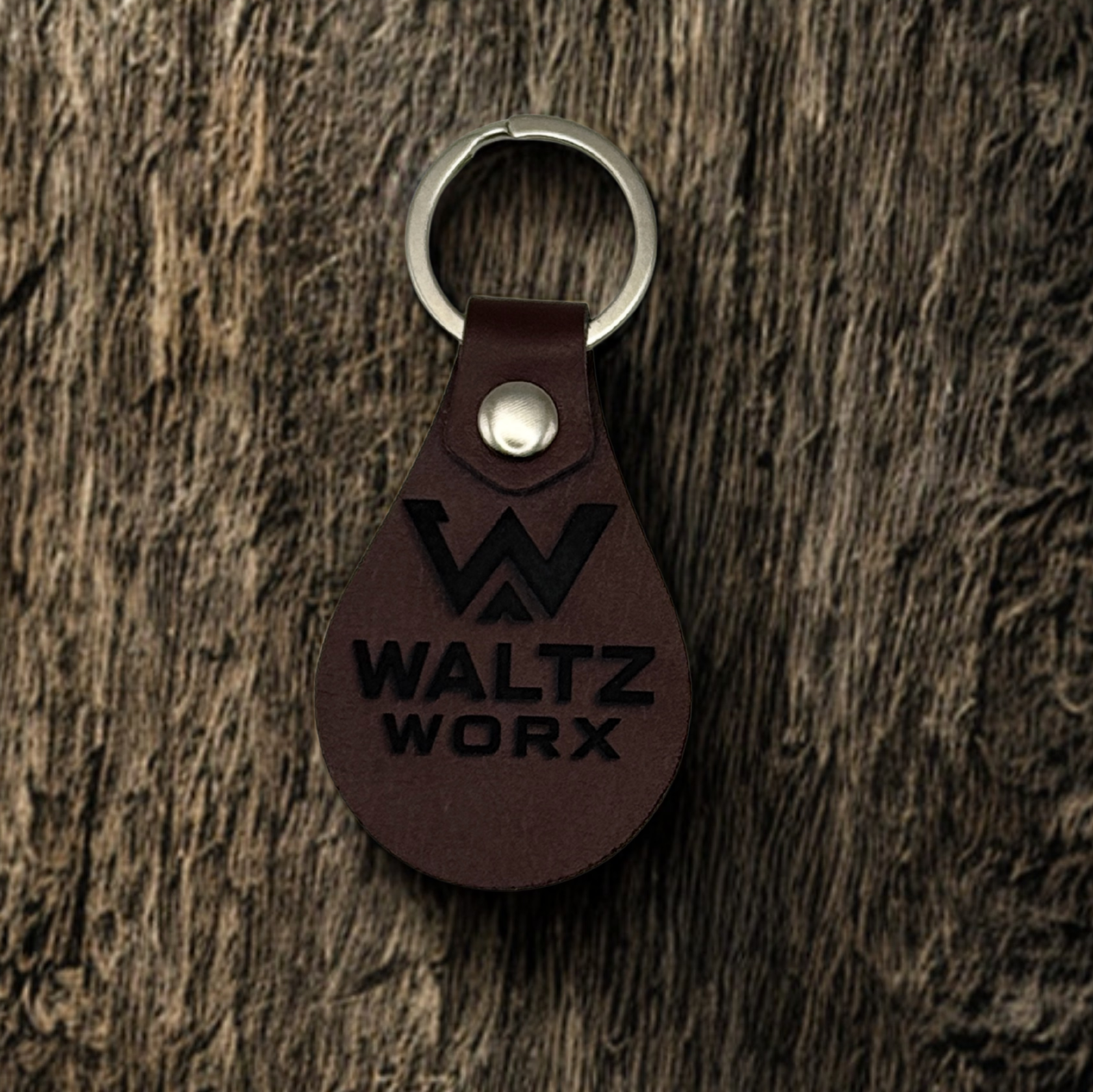 Brown leather keychain with 'Waltz Worx' logo on a wooden surface